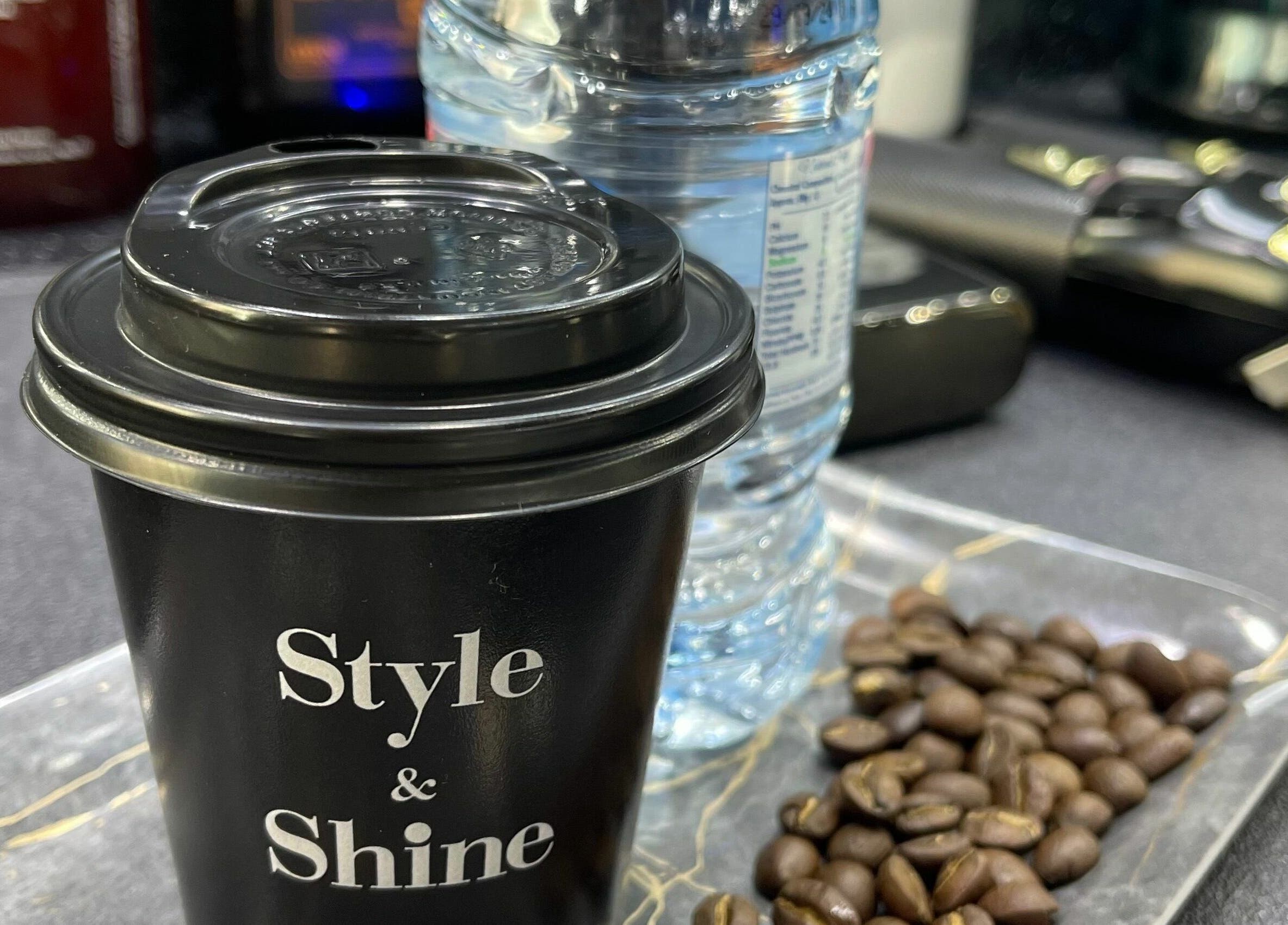 Coffee cup with 'Style & Shine Gents', water bottle, and coffee beans at Dubai, AE venue.