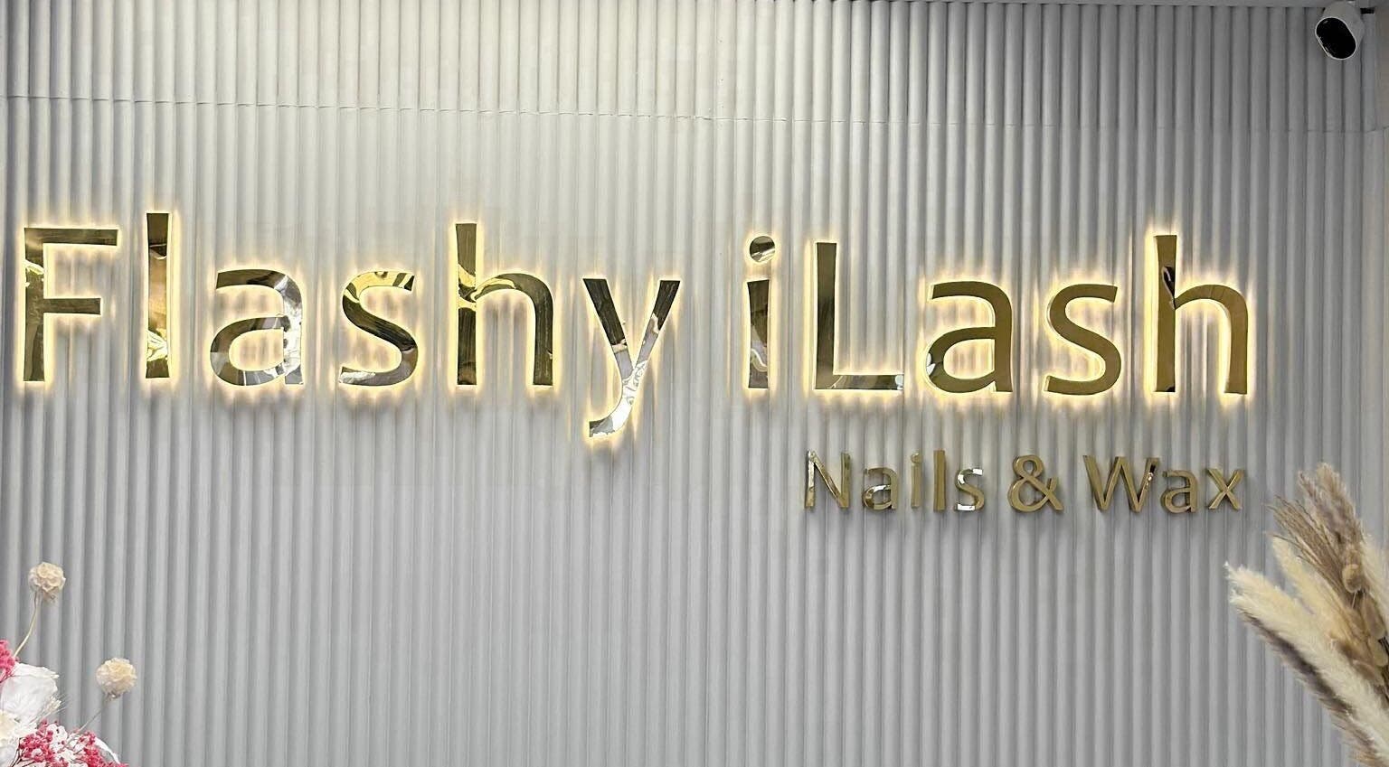 Illuminated Flashy iLash sign in Auckland, Auckland, NZ on a textured wall with decorative flowers.