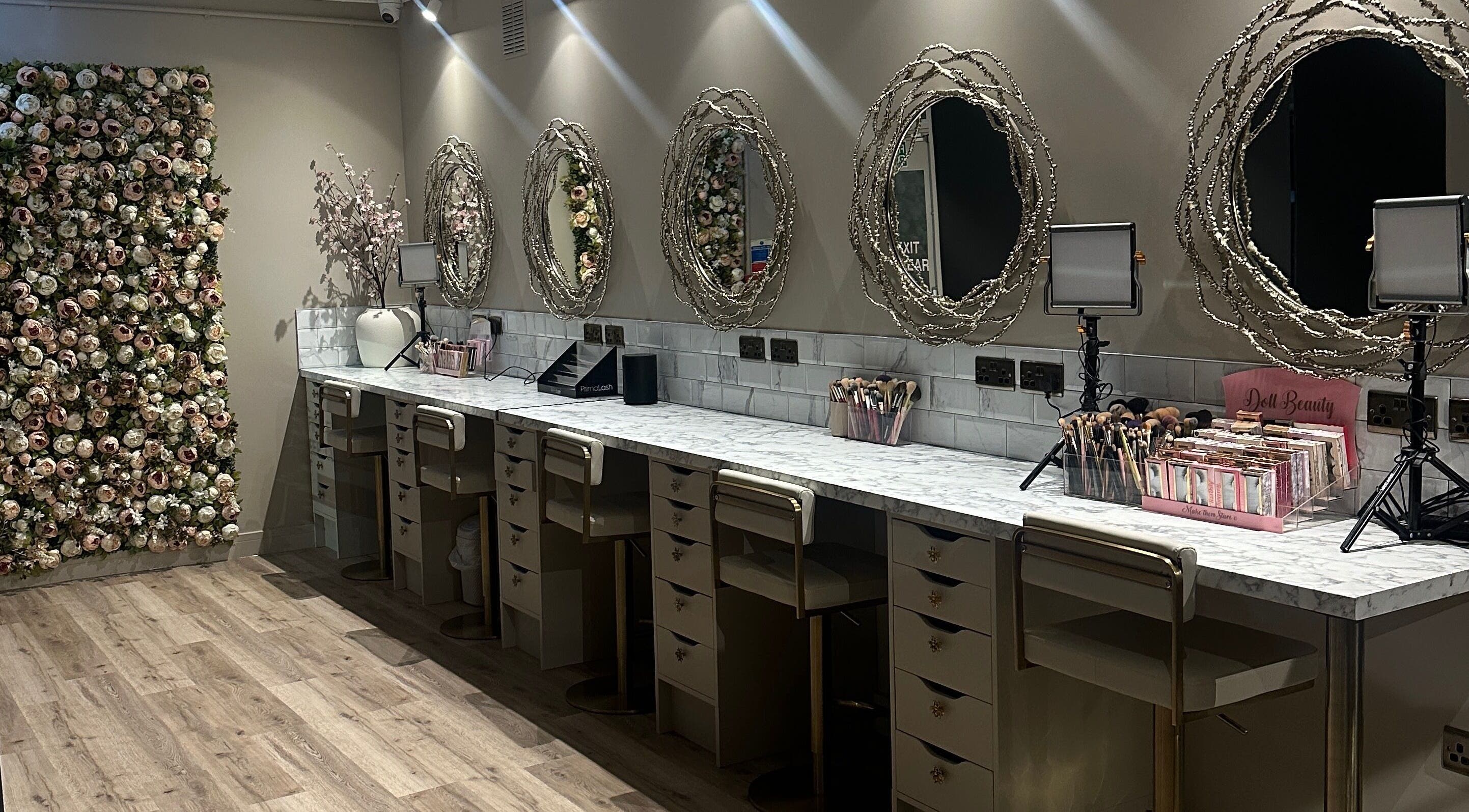 Elegant makeup station with floral wall at Blossom in Neath, Wales, GB, showcasing chic mirrors and organized beauty tools.