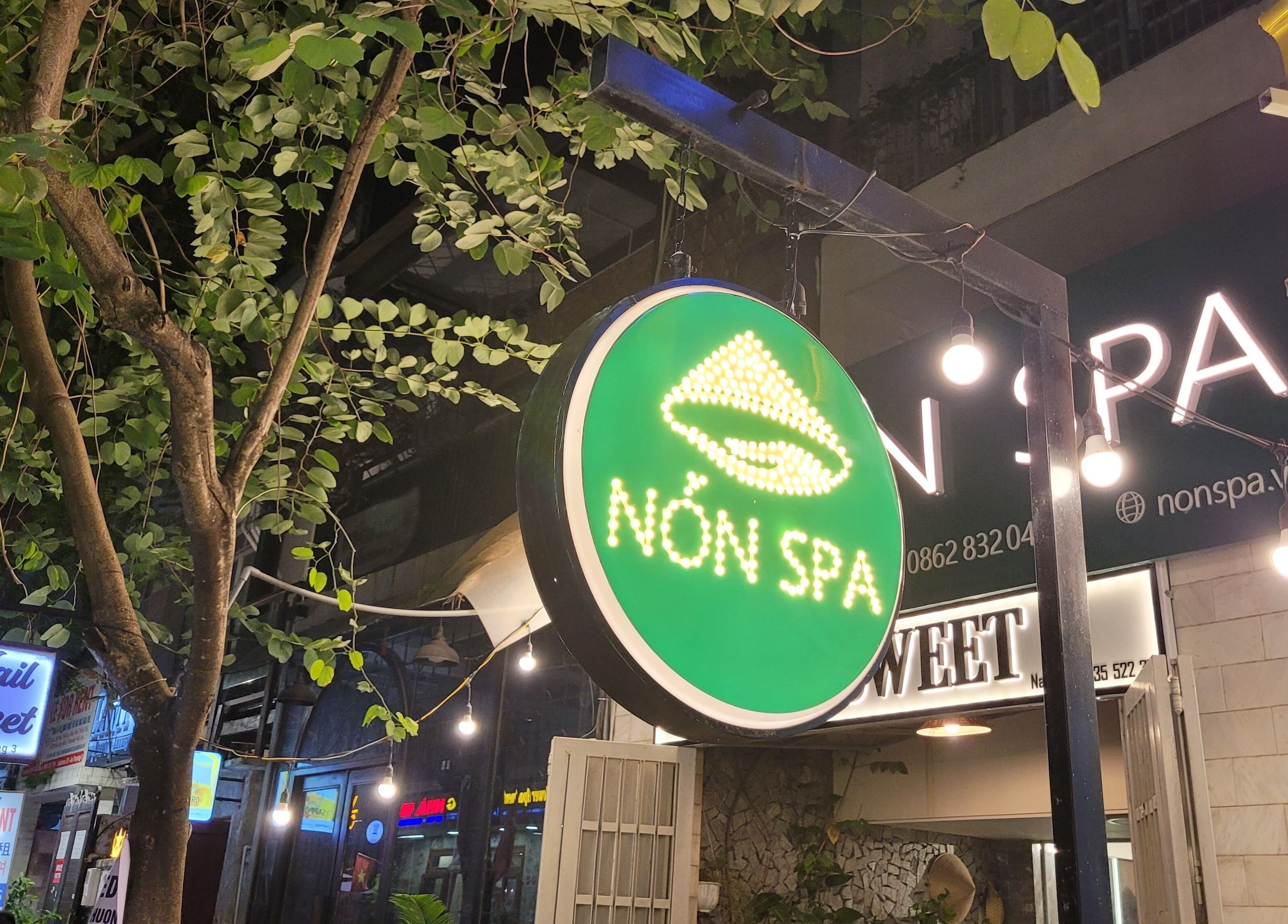Nón Spa entrance with a glowing sign, nestled among lush trees in Đà Nẵng, Đà Nẵng, VN.