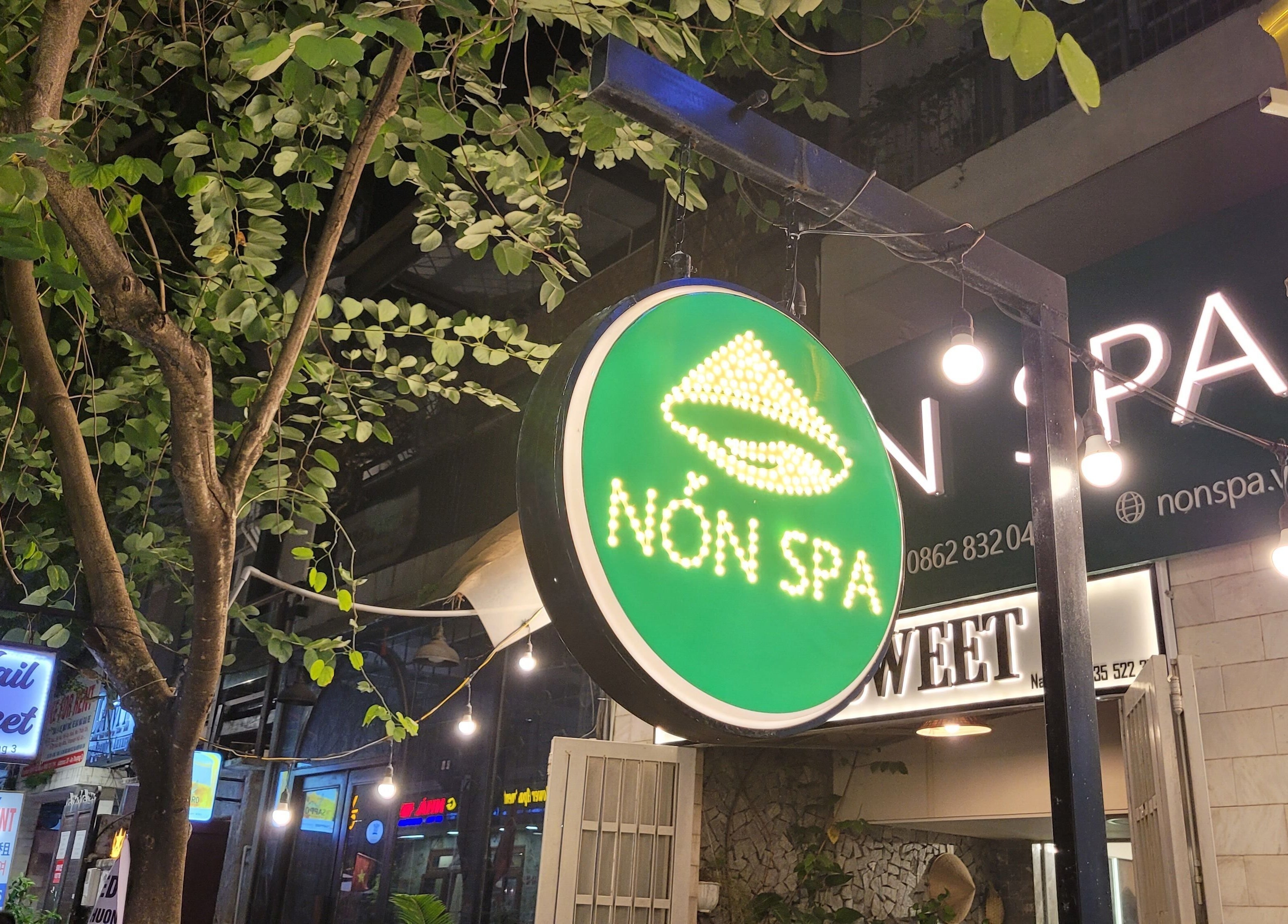 Nón Spa entrance with a glowing sign, nestled among lush trees in Đà Nẵng, Đà Nẵng, VN.