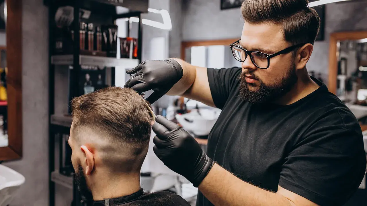 Ein Barbier verwendet einen Haartrockner, während er das ordentlich geschnittene Haar eines männlichen Kunden in einem modernen Barbiersalon stylt.