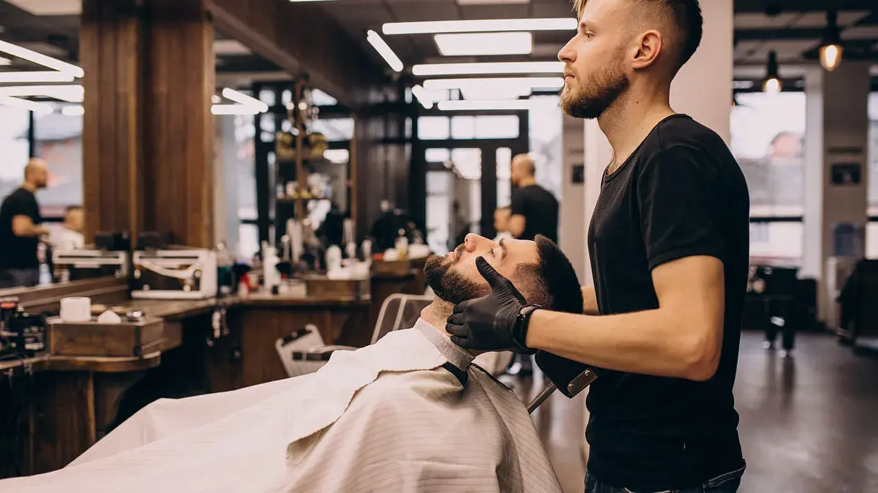 Nahaufnahme der Hände eines Friseurs, der den Kopf eines männlichen Kunden für einen professionellen Haarschnitt kämmt und schneidet.