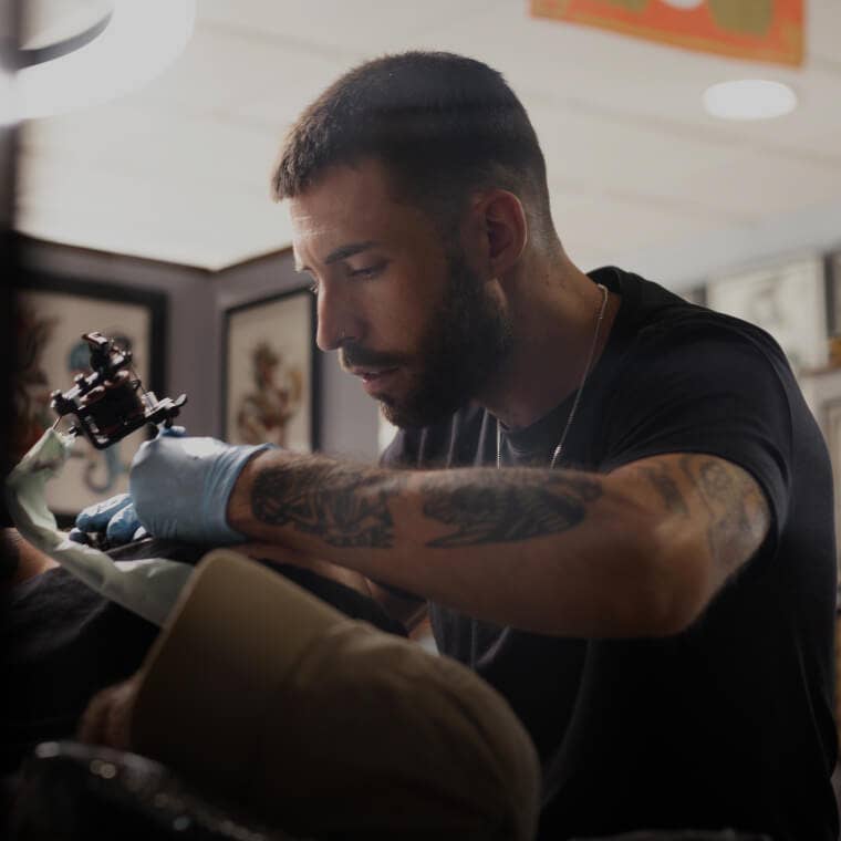 Tattoo artist creating a detailed design on a client's arm in a studio, illustrating tattoo and piercing services on Fresha.