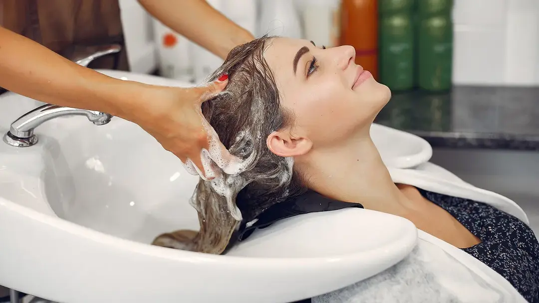 Geräumiger Salon mit warmer Beleuchtung, braunen Lederstühlen, die in einer Reihe vor großen Spiegeln angeordnet sind, vor unverputzten Ziegelwänden.
