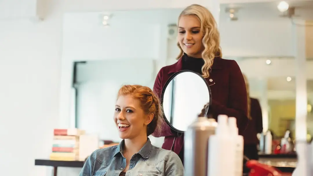 Eine Reihe eleganter, schwarzer, gepolsterter Salonstühle und hohe Spiegel auf einem hellen Holzboden in einem sauberen, minimalistischen Salonbereich.