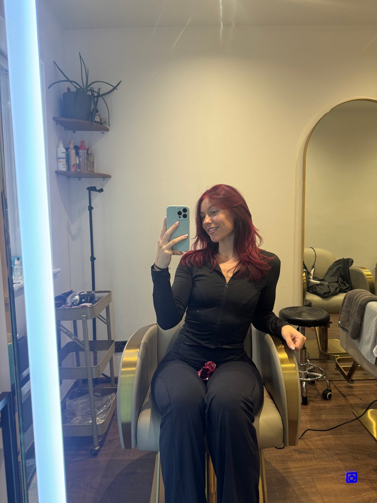 A woman sits in a sleek salon chair, capturing a selfie in a modern, stylish London salon.