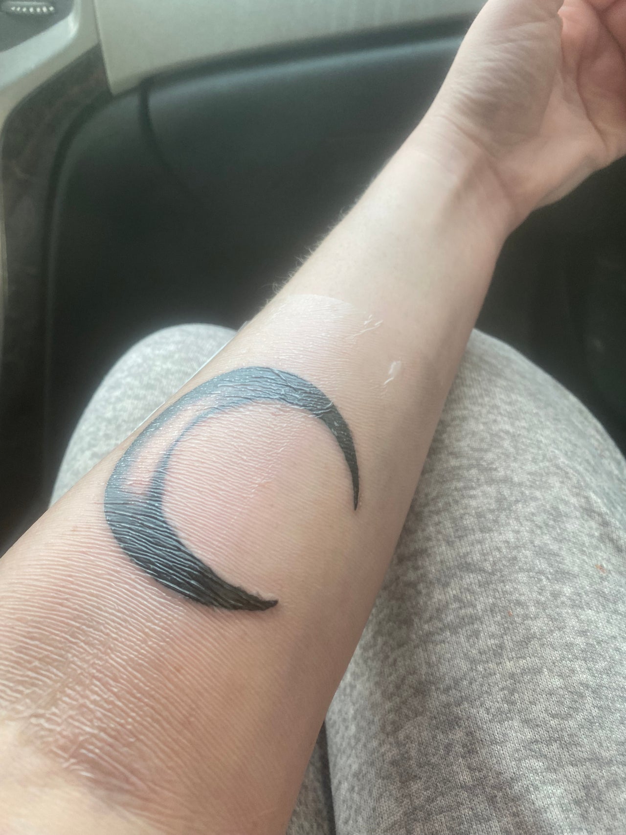 A crescent moon tattoo on a person's forearm, showcasing a fresh ink design.
