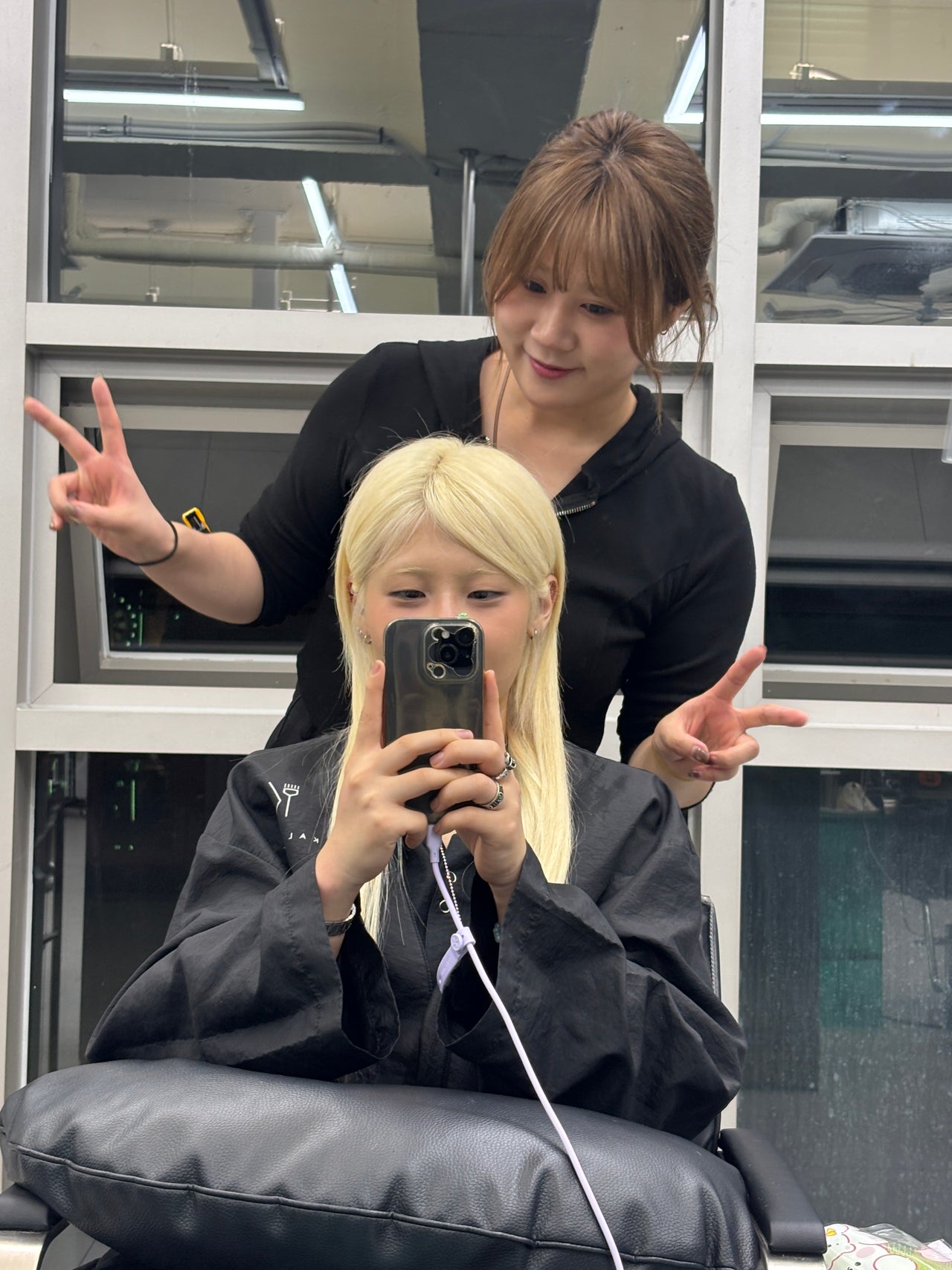 Two stylists in black shirts pose for a selfie in a modern salon interior at KKAL SALON sinsa in Seoul, South Korea.